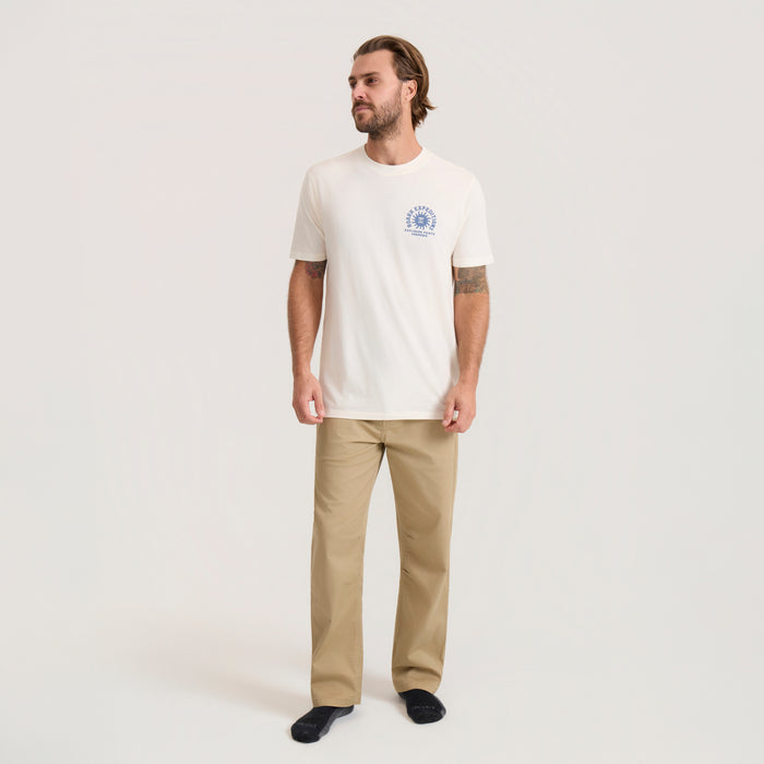 Man wearing cream Points Unknown Premium Tee with small blue circular logo on chest and khaki pants, full-body front view