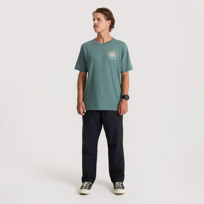Slate green short-sleeve tee with small chest graphic worn by man with black pants and canvas sneakers