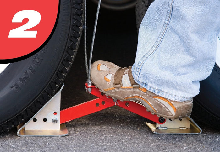 Step 2 – ONESTEP chock 84-00-4840 locking into place between trailer tires, foot activating red arm | United RV Parts