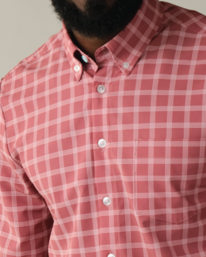 Man wearing adobe red with white windowpane shirt. Top button has blue ring.