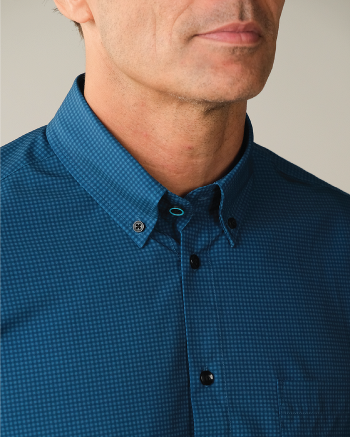 Man wearing dark blue with navy check shirt. Black buttons. Top button has blue ring. Button down collar.
