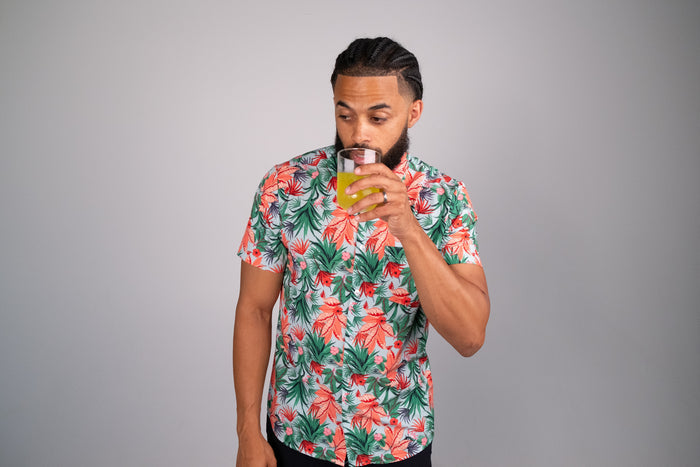 Man wearing a short sleeve Hawaiian tropical print shirt drinking orange juice out of a glass.