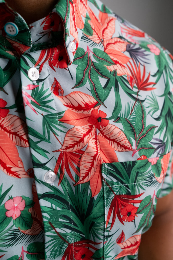 Close up of the front of a Hawaiian bright floral print shirt with buttons and one front pocket, being worn by a man.