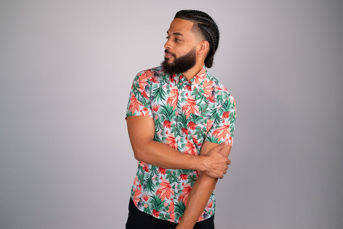 Tropical floral print shirt being worn by a model with one arm crossed over his body. Grey background.