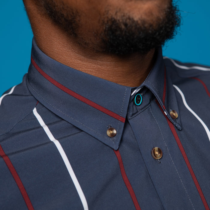 Man wearing a navy shirt with red and white stripes. Top button has blue ring