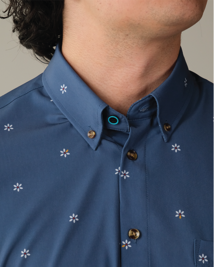 Man wearing a navy shirt with patterned white flowers, tortoise shell button, black top button with blue ring