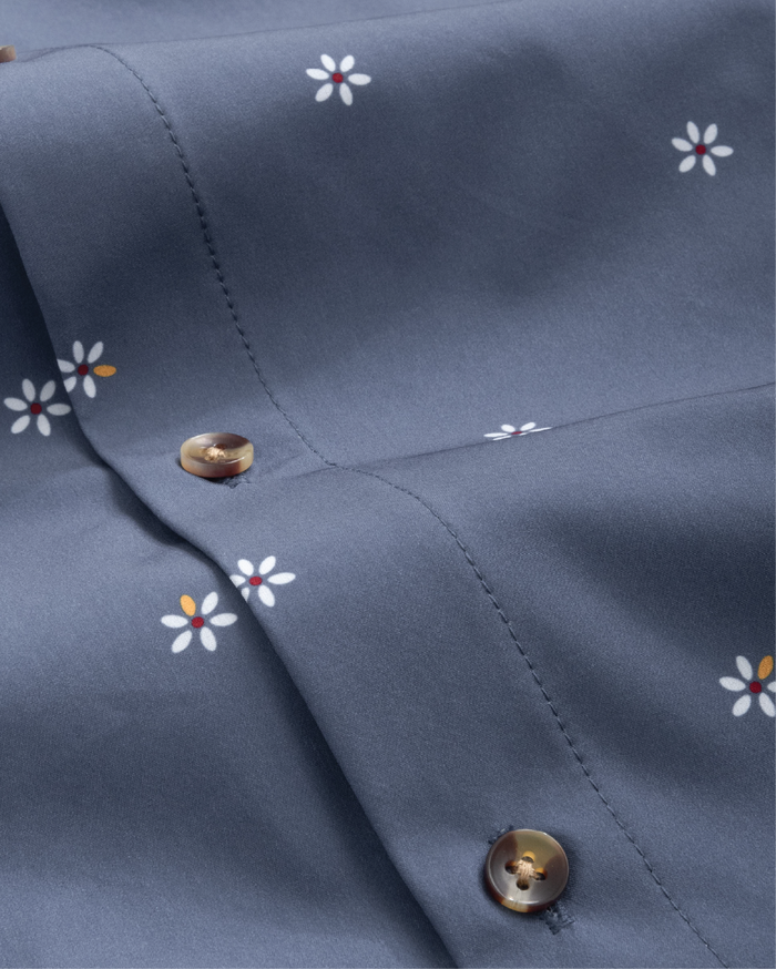 Fabric close up of navy shirt with patterned white flowers. Tortoise shell buttons