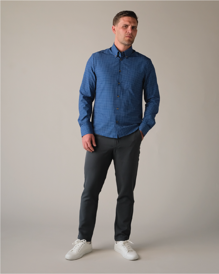 Man wearing a navy w/ white and blue check shirt with tortoise shell buttons and dark pants