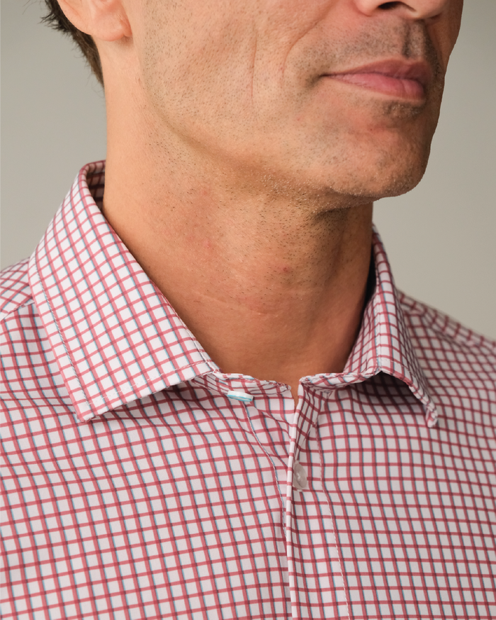 Man wearing a red and white checkered shirt with blue accent. Top button has blue ring