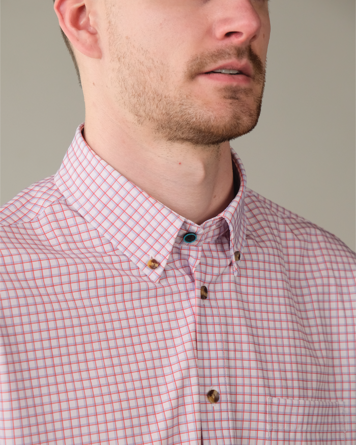 Man wearing white shirt with red and purple windowpane. Tortoise shell buttons. Top button has blue ring.