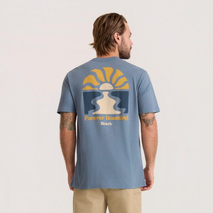 Slate blue Roaming Premium Tee with yellow sun and cream figure graphic on back, worn by man from behind