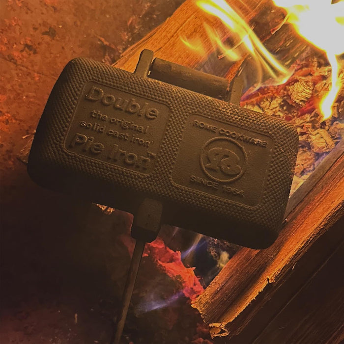 Black Cast Iron Rome Double Pie Iron 1605 Embossed Logo Close-Up Over Active Campfire Flames | United RV Parts