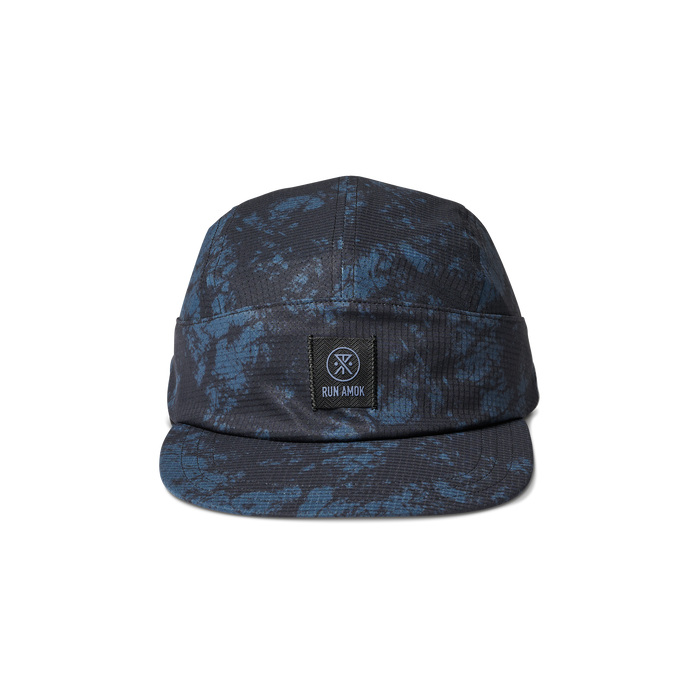 Run Amok five-panel cap in a blue and black splatter pattern, featuring a structured front panel with a woven patch logo. Perfect for outdoor adventures and urban style.