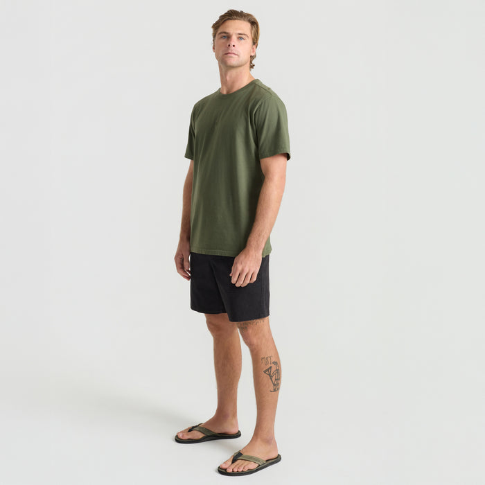 Active traveler standing in a natural setting wearing a Roark military green adventure shirt, focusing on its detailed sleeves, shoulder, and neckline.