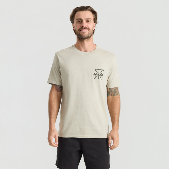Man wearing Roark active shirt and boardshorts while exploring tropical beach setting, embodying adventure and travel spirit.