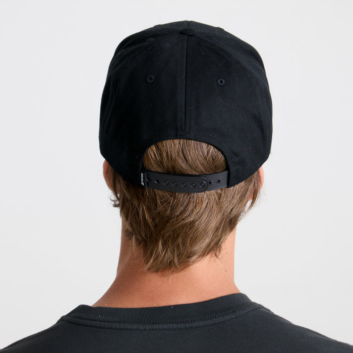 Black cricket cap placed on a rustic wooden surface, evoking a sense of adventure and travel, by Roark.