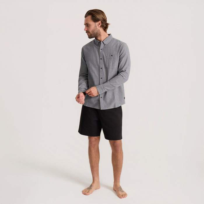 Man wearing gray chambray button-up shirt with black shorts, shown in full-length profile view on neutral background