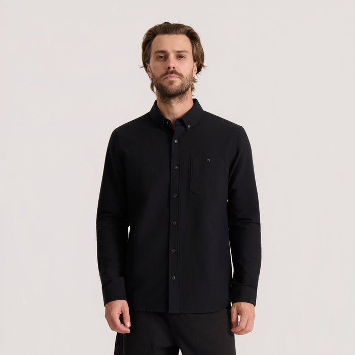 Black Scholar Chambray Button Up Shirt worn by man, featuring long sleeves, chest pocket, and button front closure