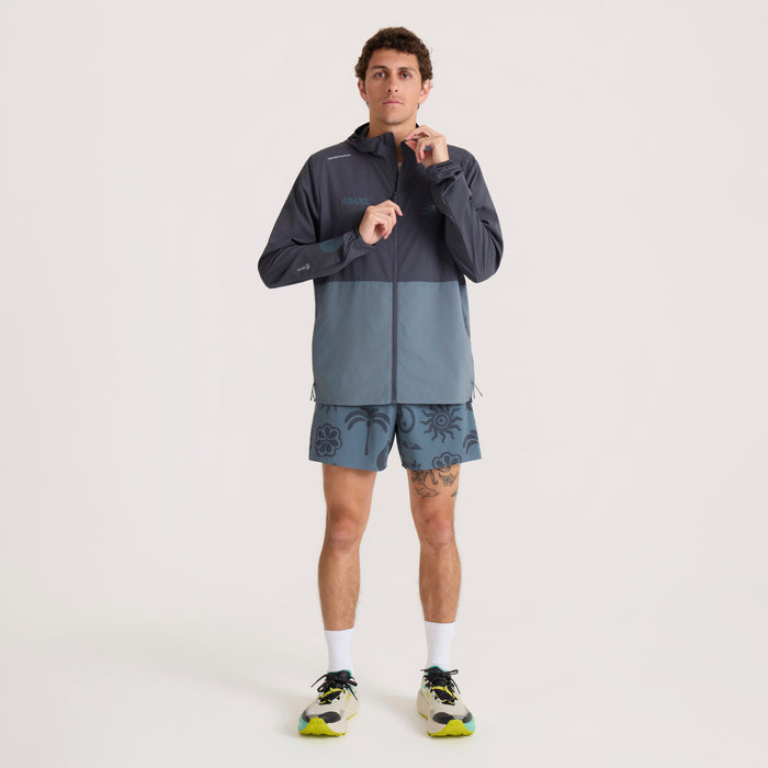 Man wearing Roark Second Wind Jacket in ebony and slate colorblock with matching patterned shorts and white socks