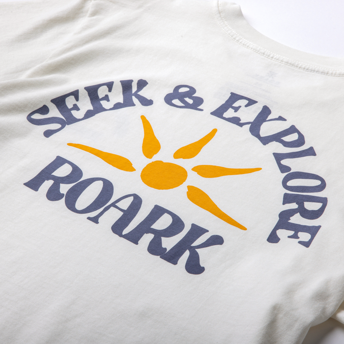 Seek & Explore Premium Tee in off white with navy text and golden sun graphic on chest, flat lay detail view