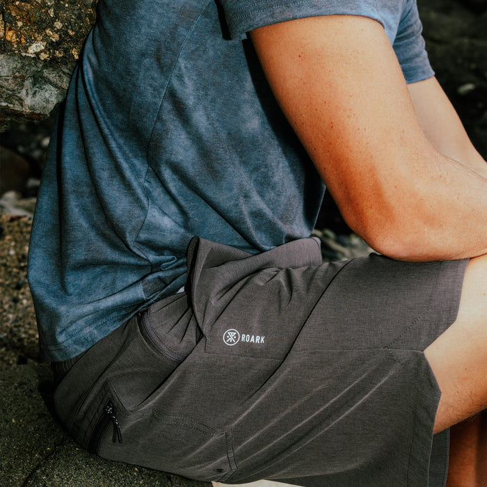 Charcoal heather Serrano shorts with white Roark logo worn by a man sitting outdoors in a blue shirt, detail view of fit and fabric