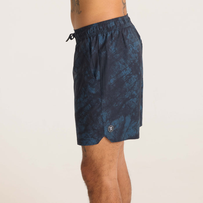 Model walking in navy tie-dye swim shorts, styled with vibrant sneakers, showcasing movement and flexibility for active wear.