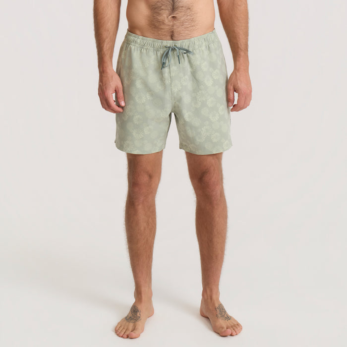 Man in Roark boardshorts standing by the ocean, embodying a carefree and adventurous spirit