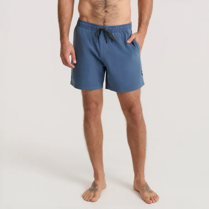 Shirtless man wearing blue Shorey 16" Trunks in washed indigo with drawstring, standing barefoot against white background