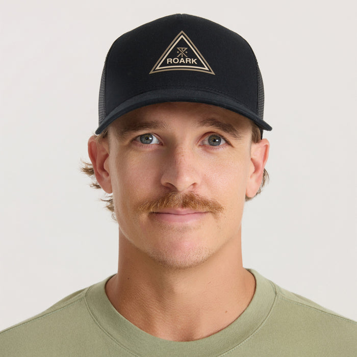 Black Roark Station Trucker Tricamp Snapback Hat with tan triangle logo, worn by man on beige background