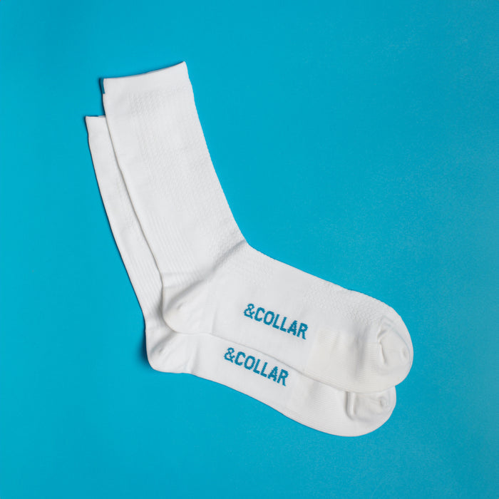 White dress socks with a light blue &Collar logo on the arch of the socks