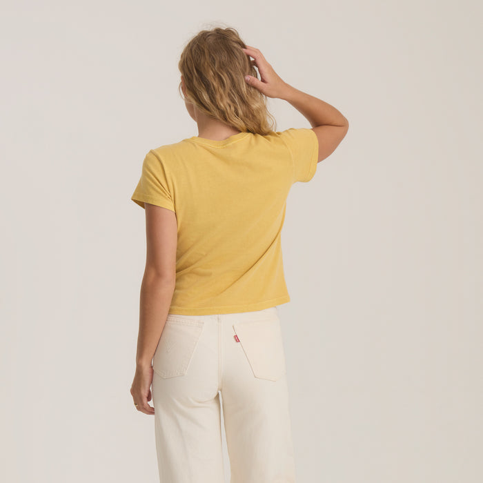 Woman wearing yellow short-sleeve t-shirt and cream jeans, shown from back view against neutral background