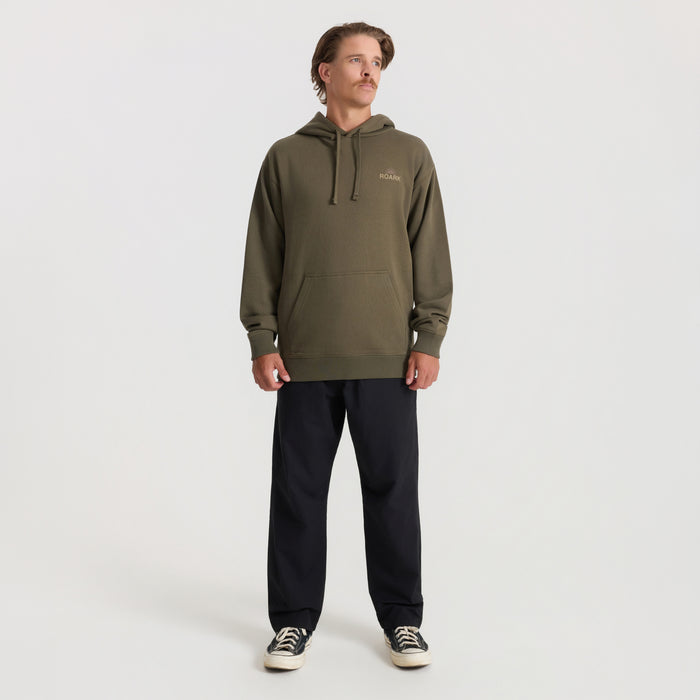 Man wearing military green Roark Tri Camp Hoodie with kangaroo pocket, styled with black pants and canvas sneakers