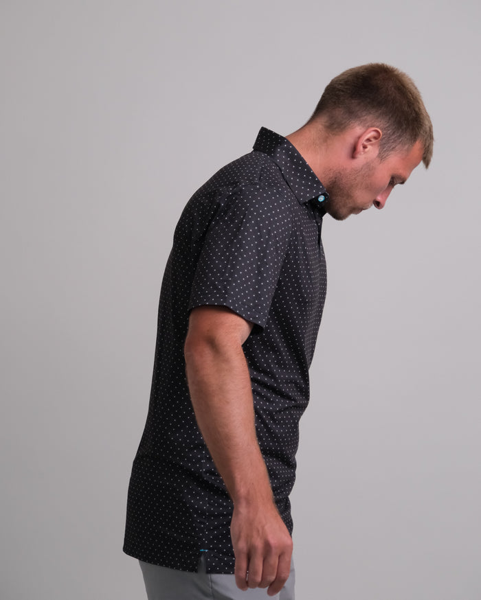 Man wearing a black with white polka dots short sleeve polo shirt against a gray background