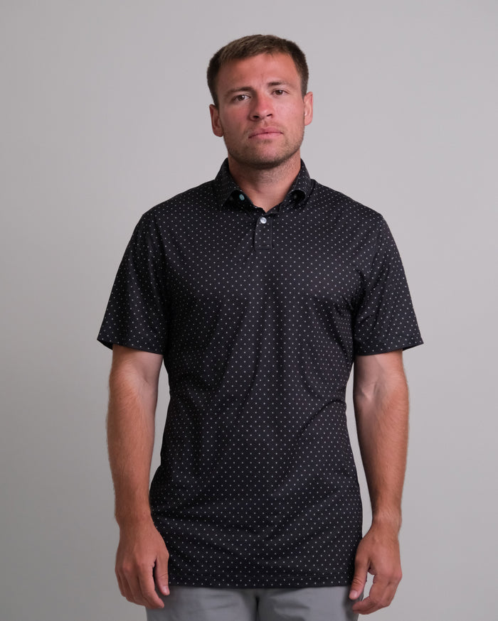 Man wearing a black with white polka dots short sleeve polo shirt against a plain background