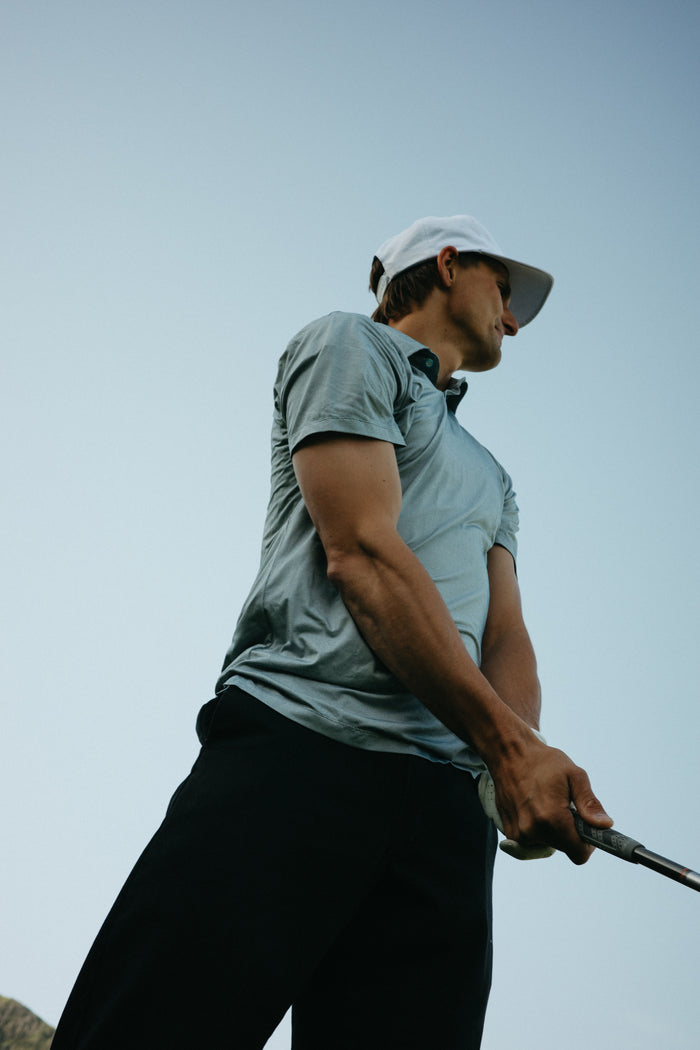 Man playing golf with a clear sky background in a steel gray short sleeve polo shirt