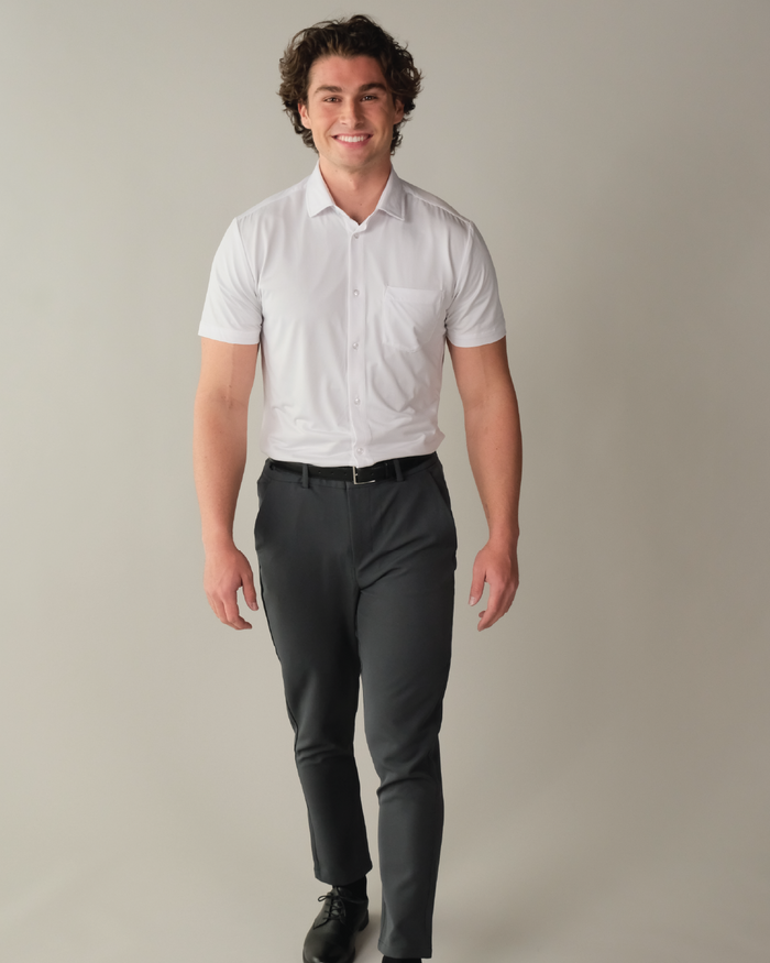 A man walking in a white short sleeve button up collared shirt with a beige background.