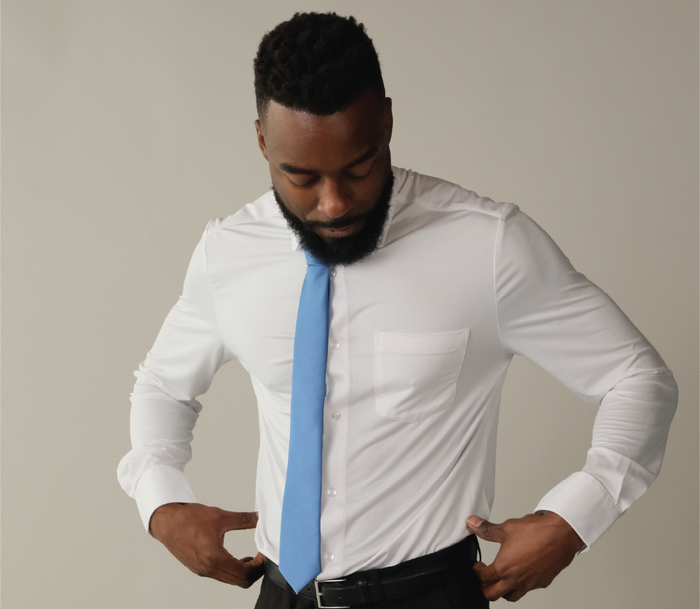 A man wearing a white long sleeve button up shirt with a light blue tie and black pants.