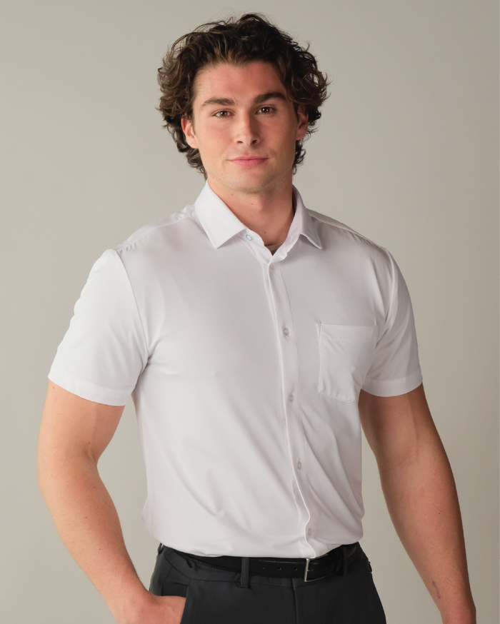 Close up of man wearing a white short sleeve button up dress shirt with a beige background.
