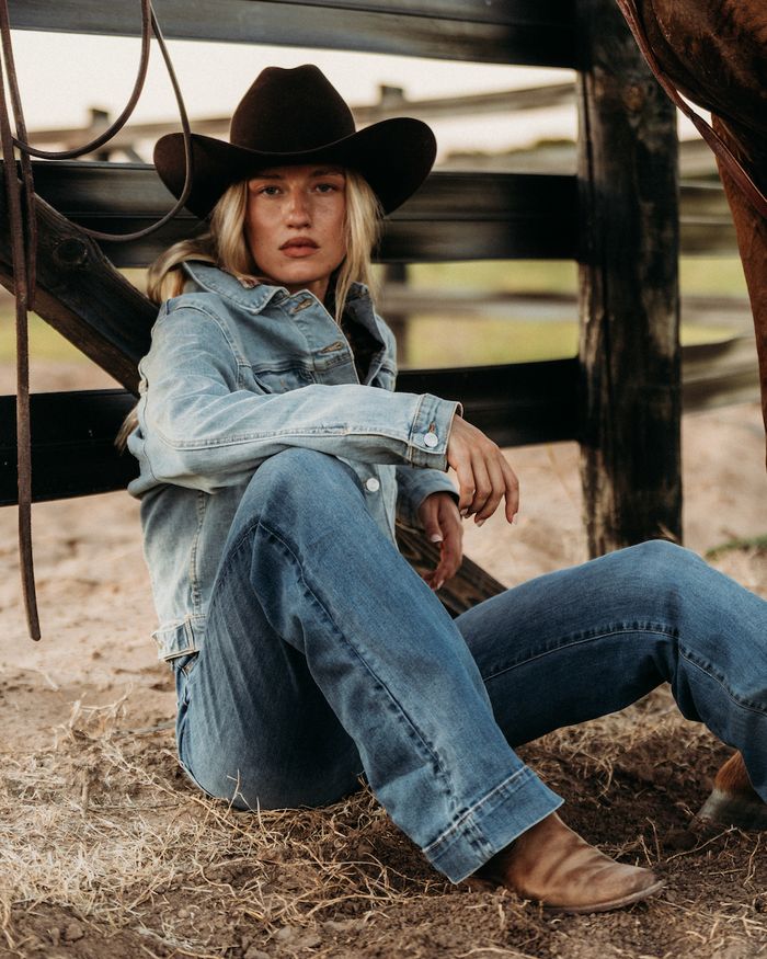 Cowgirl sitting down underneath horse in all denim.