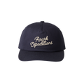 Navy snapback hat with cream embroidered Roark Expeditions script logo on front, flat lay view against white background