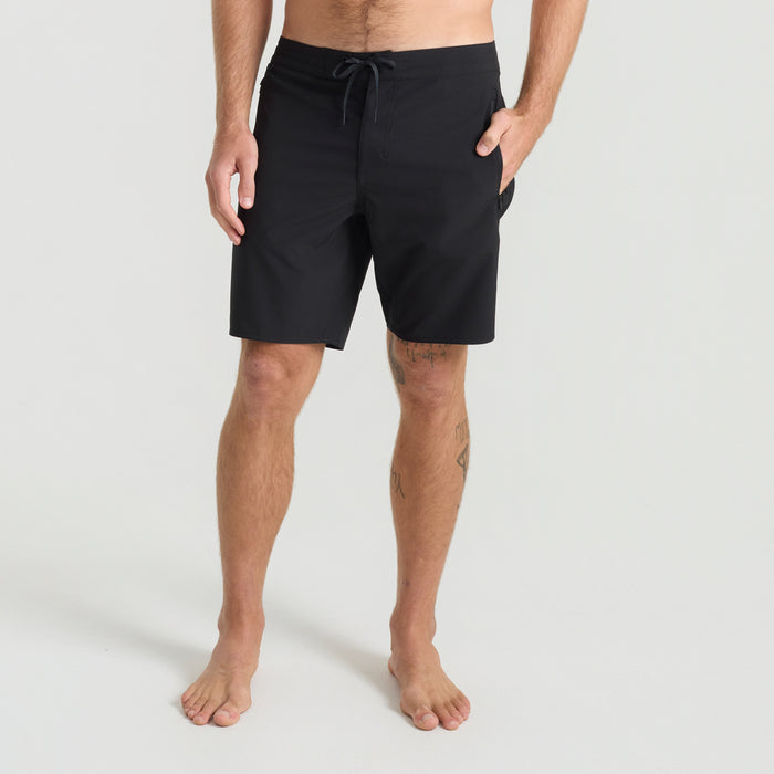 Adventurous man in black boardshorts stands barefoot on the beach, showcasing a relaxed and rugged outdoor lifestyle ideal for adventure travel.