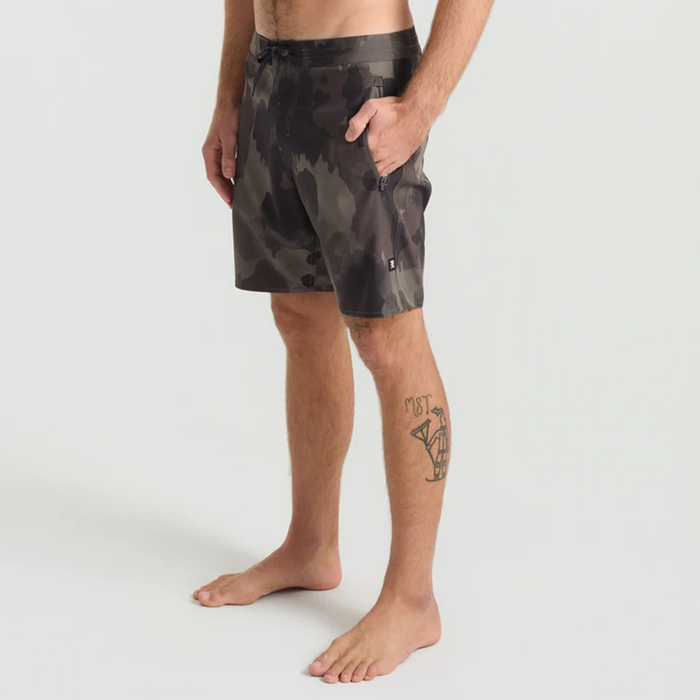 Active male wearing colorful boardshorts standing in shallow water with a focus on calf and feet, embodying the spirit of adventure and travel.