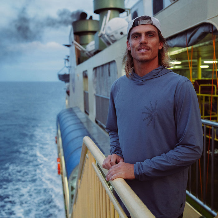 Man wearing Neptune blue Venture UPF hoodie on ship deck with ocean horizon in background, lifestyle shot
