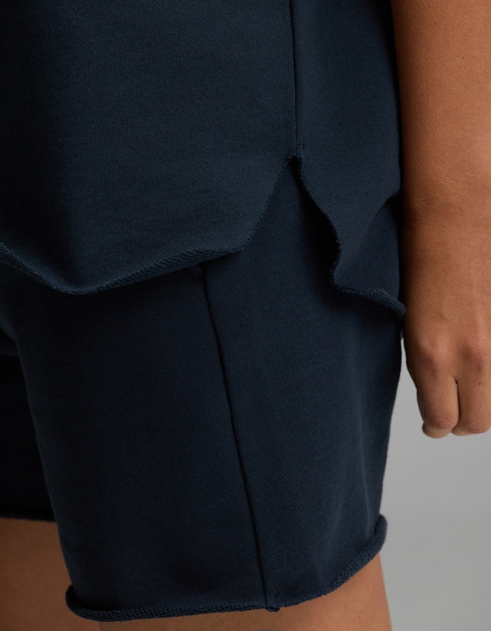A close-up of a person’s hand resting by their side, wearing the Cozy Earth Women’s Chelsea Short Sleeve top in dark blue paired with matching shorts featuring raw, unfinished edges.|Color:Eclipse